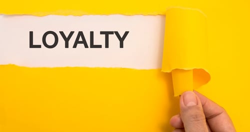 Käsi repii keltaista taustapaperia, jonka alta paljastuu valkoisella pohjalla oleva teksti LOYALTY kuvaamassa asiakasuskollisuuden strategioita.